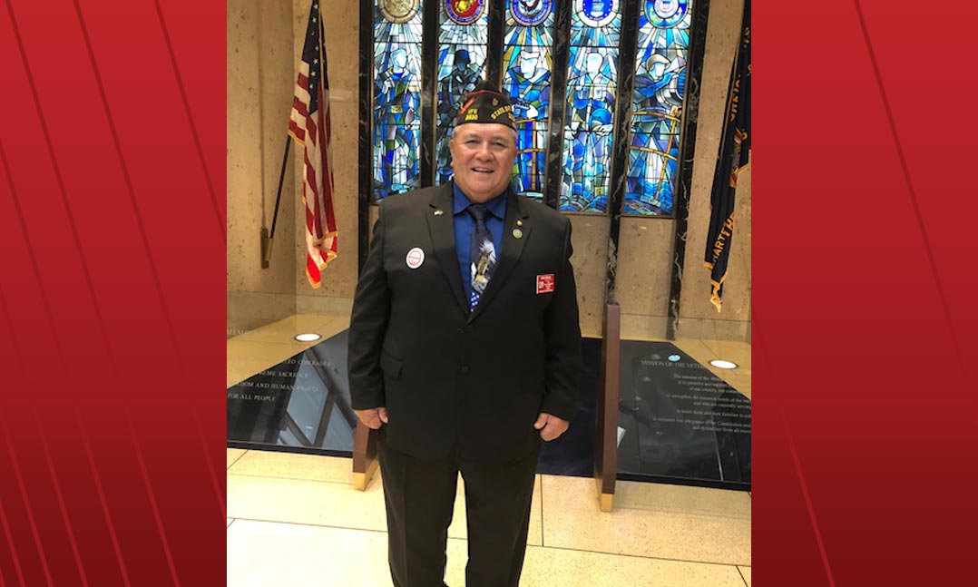 Commander of Post 3830 in Pāhoa, Hawaii, and Department Service Officer of Hawaii Ben Fuata stands before five stained-glass windows
